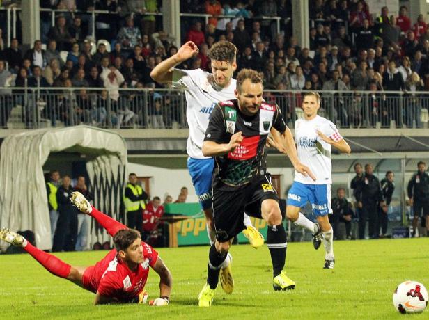 Ein Fußballspieler läuft mit dem Ball, während der Torwart auf dem Rasen liegt.
