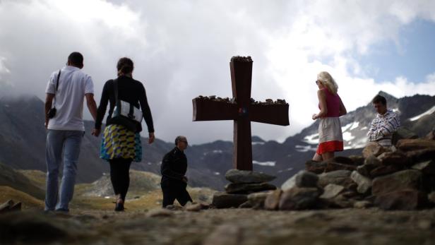 Mehrere Personen besuchen ein Gipfelkreuz in den Bergen.