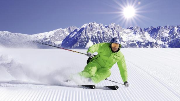 Ein Skifahrer in grüner Kleidung fährt eine schneebedeckte Piste hinunter.