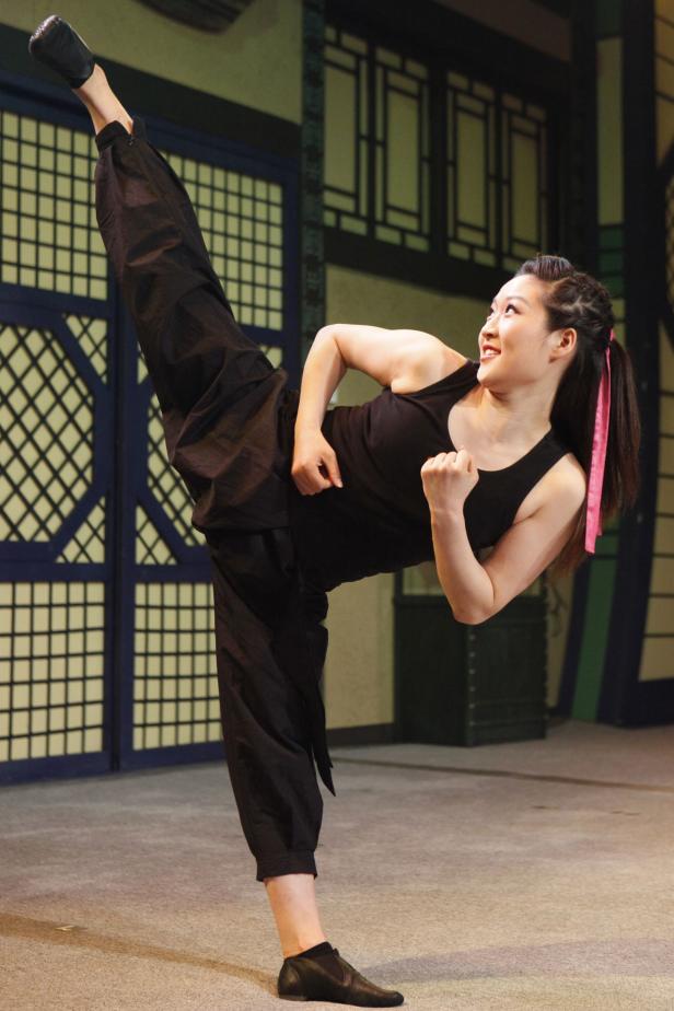 Eine Frau in schwarzer Sportkleidung führt einen hohen Tritt aus.