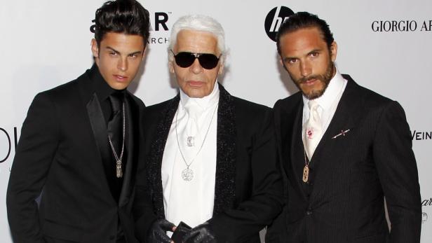 Karl Lagerfeld posiert mit zwei jungen Männern in Anzügen.