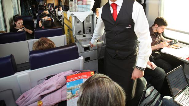 Ein Steward schiebt einen Servierwagen durch einen Zug voller Reisender.