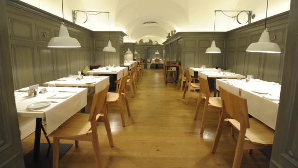 Ein leerer Speisesaal mit gedeckten Tischen und Holzstühlen.