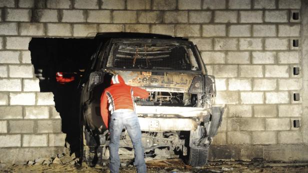 Ein ausgebranntes Auto steckt in einem Loch in einer Ziegelmauer.