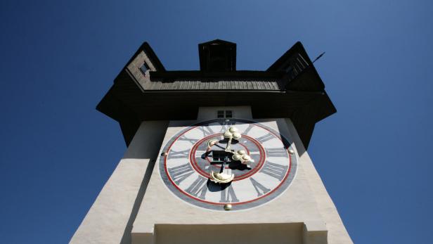 Der Grazer Uhrturm von unten gegen einen blauen Himmel fotografiert.