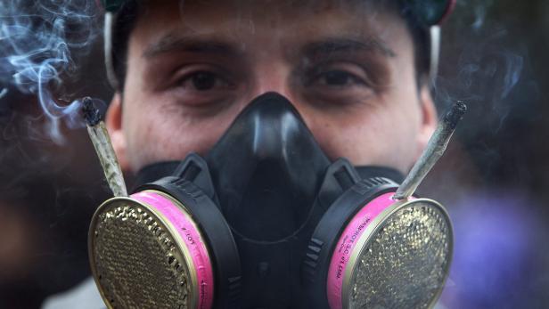 Ein Mann mit Gasmaske, in deren Filtern zwei Joints stecken.