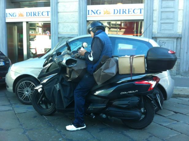 Ein Rollerfahrer mit Helm und Weste sitzt auf seinem Roller vor einer ING Direct Filiale.