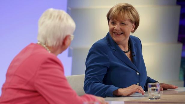 Angela Merkel lächelt während eines Interviews mit einer Frau in einem rosafarbenen Blazer.