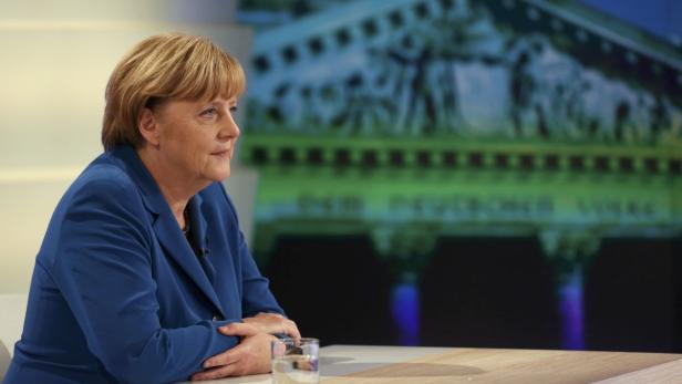 Angela Merkel sitzt an einem Tisch vor einem unscharfen Hintergrund.