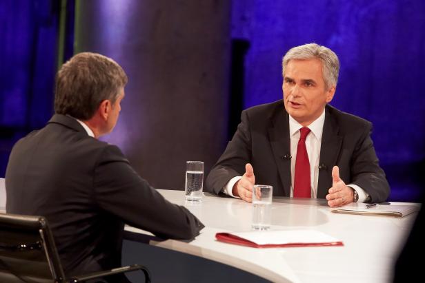 Zwei Männer sitzen an einem Tisch und diskutieren vor blauem Hintergrund.