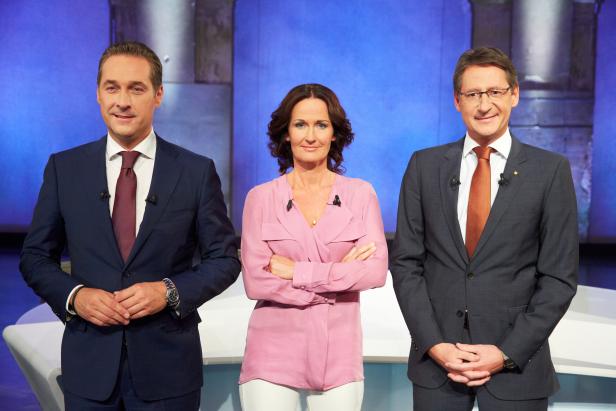 Drei Personen stehen vor einem blauen Hintergrund im Studio.