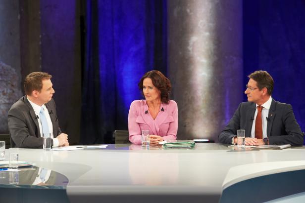 Drei Personen sitzen an einem Tisch während einer Podiumsdiskussion.