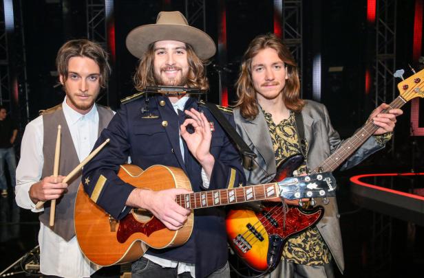 Eine dreiköpfige Band posiert mit Gitarre, Bass und Schlagzeugstöcken.