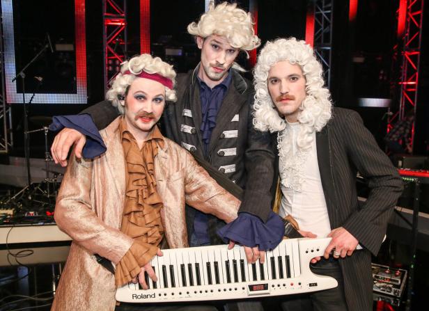 Drei Männer in historischen Kostümen und Perücken posieren mit einem Roland-Keyboard.