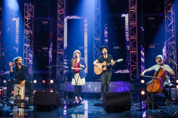 Eine Band tritt auf einer Bühne mit Gitarre, Cello, Xylophon und Cajón auf.
