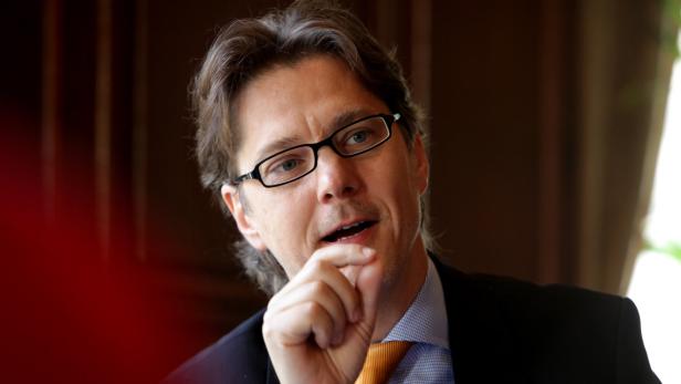 Ein Mann mit Brille und Anzug gestikuliert mit der Hand.