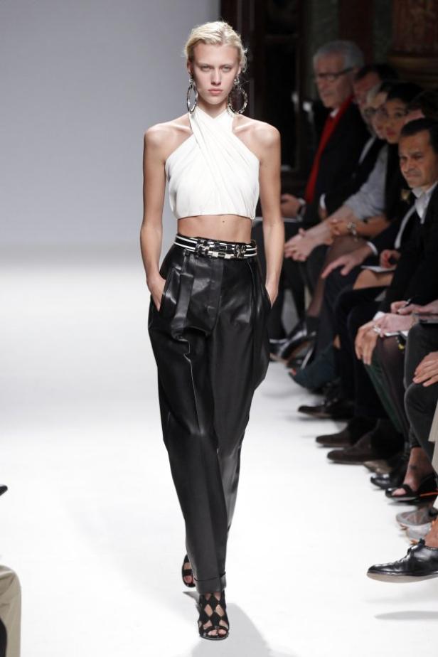 Ein Model präsentiert ein weißes Top und eine schwarze Hose auf dem Laufsteg.