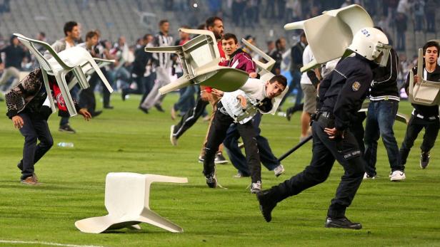 Während einer Auseinandersetzung auf einem Fußballfeld werfen Menschen mit Stühlen um sich.