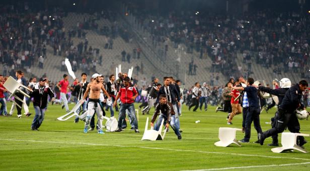 Auf dem Rasen eines Stadions kommt es zu Ausschreitungen mit Stühlen und Polizisten.