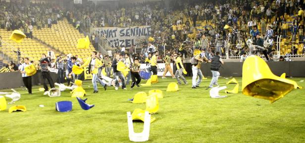 Zuschauer werfen mit Stühlen auf das Spielfeld während eines Fußballspiels.