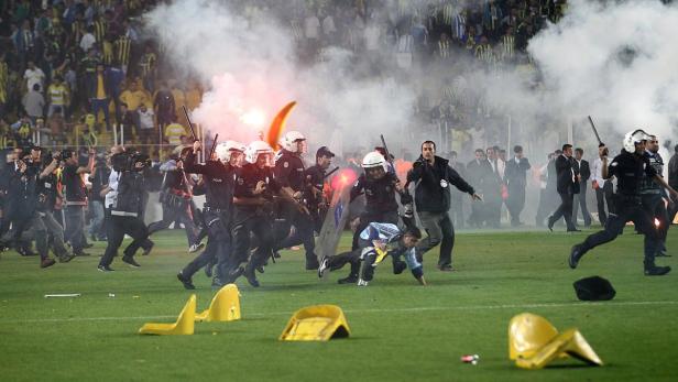 Polizisten verfolgen einen Mann auf dem Spielfeld, während Rauch und Bengalos aufsteigen.