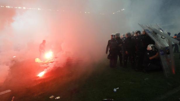 Polizisten stehen inmitten von Rauch und Bengalfeuer in einem Stadion.