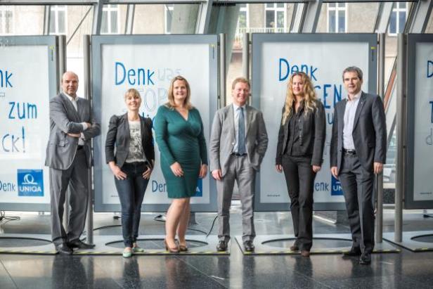 Eine Gruppe von sechs Personen posiert vor Werbetafeln der UNIQA Versicherung.
