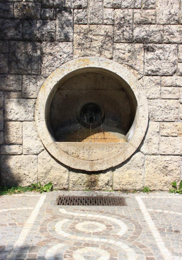 Ein kreisförmiger Brunnen ist in eine Steinmauer eingelassen.