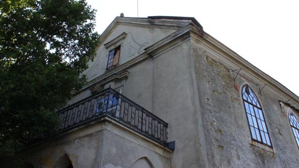 Ein älteres, graues Gebäude mit einem Balkon und hohen Fenstern.