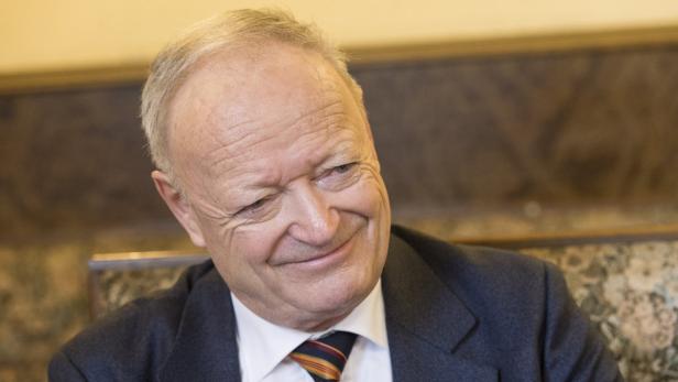 Ein älterer Mann mit Anzug und Krawatte lächelt verschmitzt.