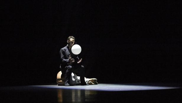 Ein Mann sitzt auf einer anderen Person und balanciert einen weißen Ball.