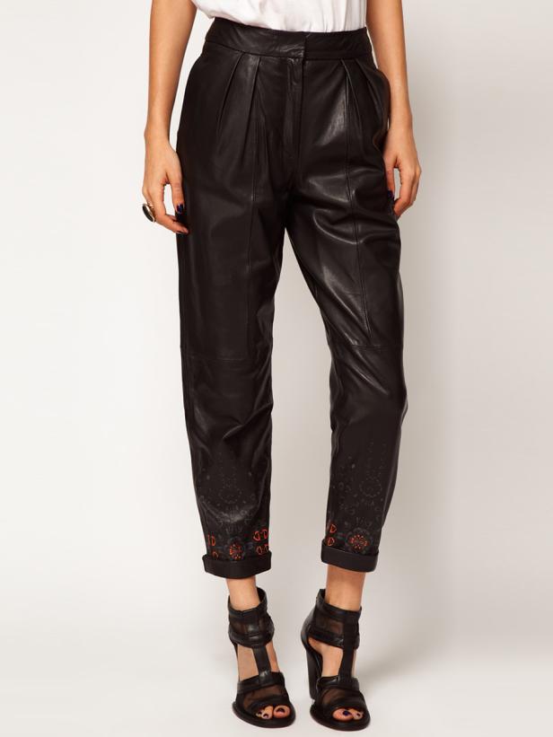 Eine Frau trägt eine schwarze Lederhose mit hochgekrempelten Beinen und schwarzen Sandalen.