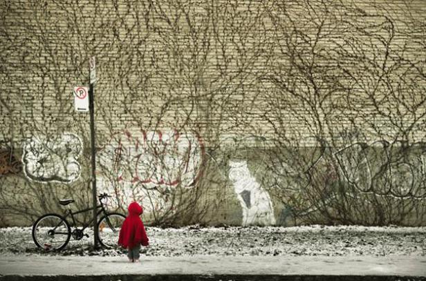 Ein kleines Kind in roter Jacke steht vor einer mit Graffiti bedeckten Mauer.