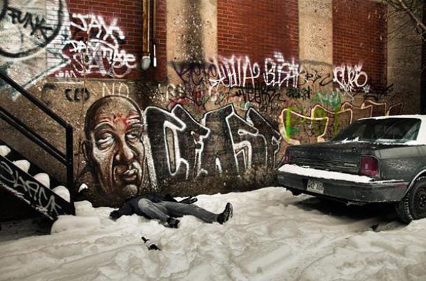 Eine Person liegt im Schnee vor einer mit Graffiti bedeckten Wand und einem Auto.