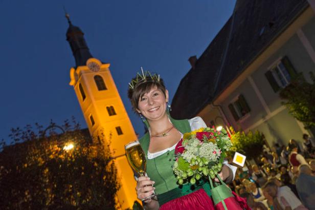 Eine junge Frau in Tracht hält ein Bier und einen Blumenstrauß in der Hand.