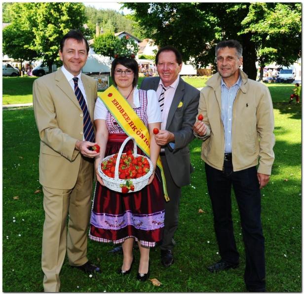 Die Erdbeerkönigin präsentiert einen Korb voller Erdbeeren, umgeben von drei Männern.