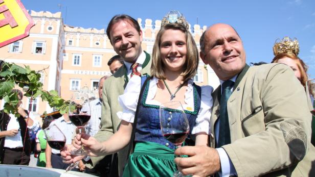 Eine Weinkönigin mit Krone und zwei Männern halten Weingläser in der Hand.