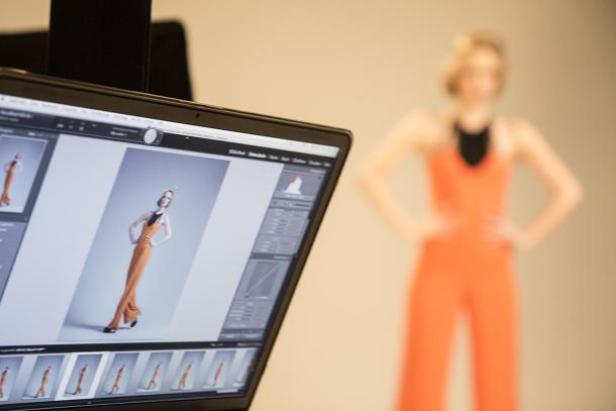 Ein Laptop zeigt ein bearbeitetes Foto eines Models in einem orangefarbenen Overall.