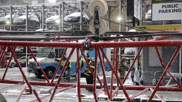 Im Schneefall arbeiten Bauarbeiter an einem Kran vor einem Parkhaus.