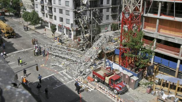 Ein eingestürzter Baukran liegt auf einer städtischen Straße, umgeben von Trümmern und Einsatzkräften.