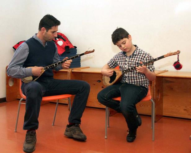 Ein Mann und ein Junge sitzen auf Stühlen und spielen ein Saiteninstrument.