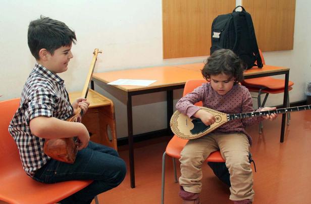 Zwei Kinder sitzen auf Stühlen und spielen ein Saiteninstrument.