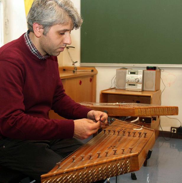 Ein Mann stimmt ein traditionelles Hackbrett, ein Saiteninstrument.