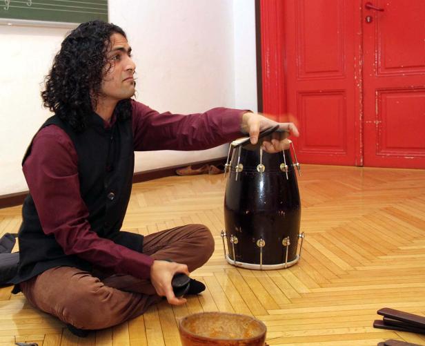 Ein Mann sitzt auf dem Boden und spielt ein Musikinstrument.