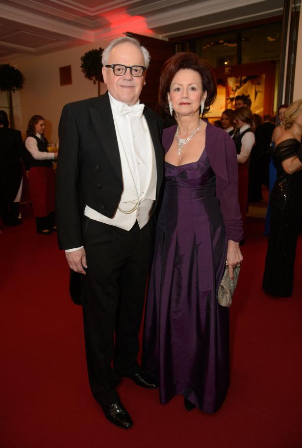 Ein Mann im Frack und eine Frau im lila Abendkleid posieren auf einem roten Teppich.