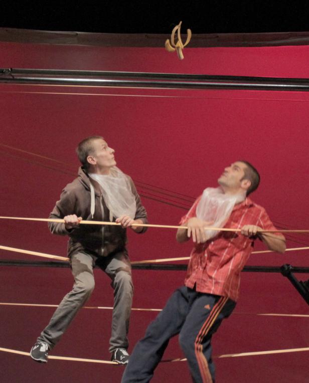 Zwei Männer auf einer Bühne mit Plastiktüten um den Hals schauen auf eine Banane in der Luft.