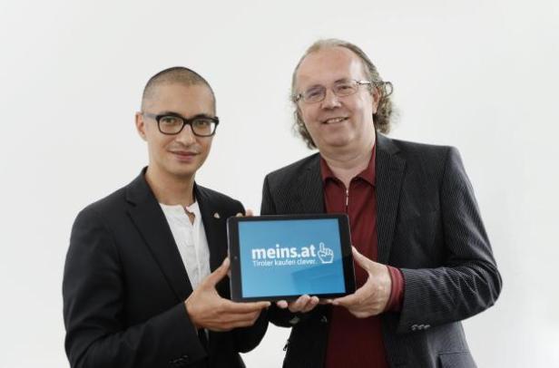 Zwei Männer präsentieren ein Tablet mit der Aufschrift „meins.at“.