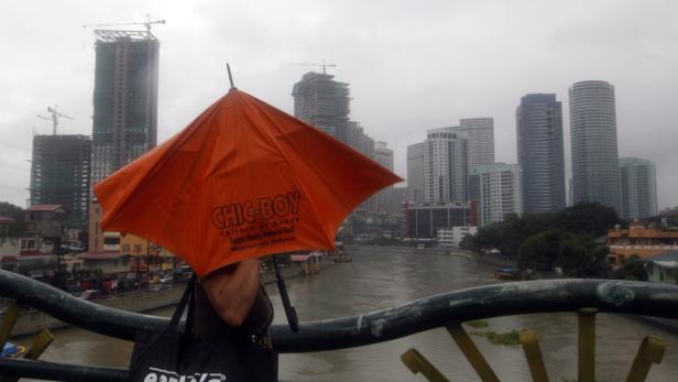 Eine Person steht mit einem orangefarbenen „Chic-Boy“-Regenschirm vor einer Skyline in Meycauayan, Bulacan.