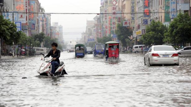 Eine Frau fährt mit einem Motorroller durch eine überflutete Straße in einer chinesischen Stadt.
