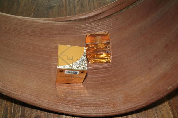 Ein goldener Flakon und die dazugehörige Verpackung liegen in einer braunen Schale.